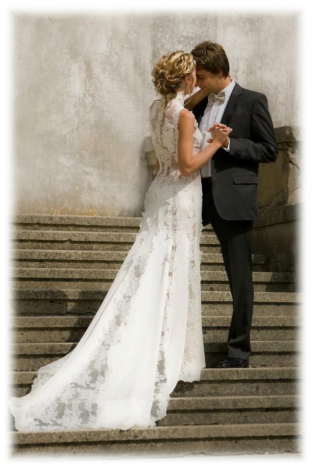 Bride and groom on stone steps, with the lace gown and train shown from behind