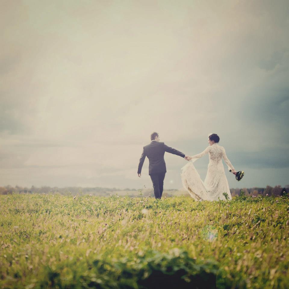 Bride and groom walking hand in hand across a field