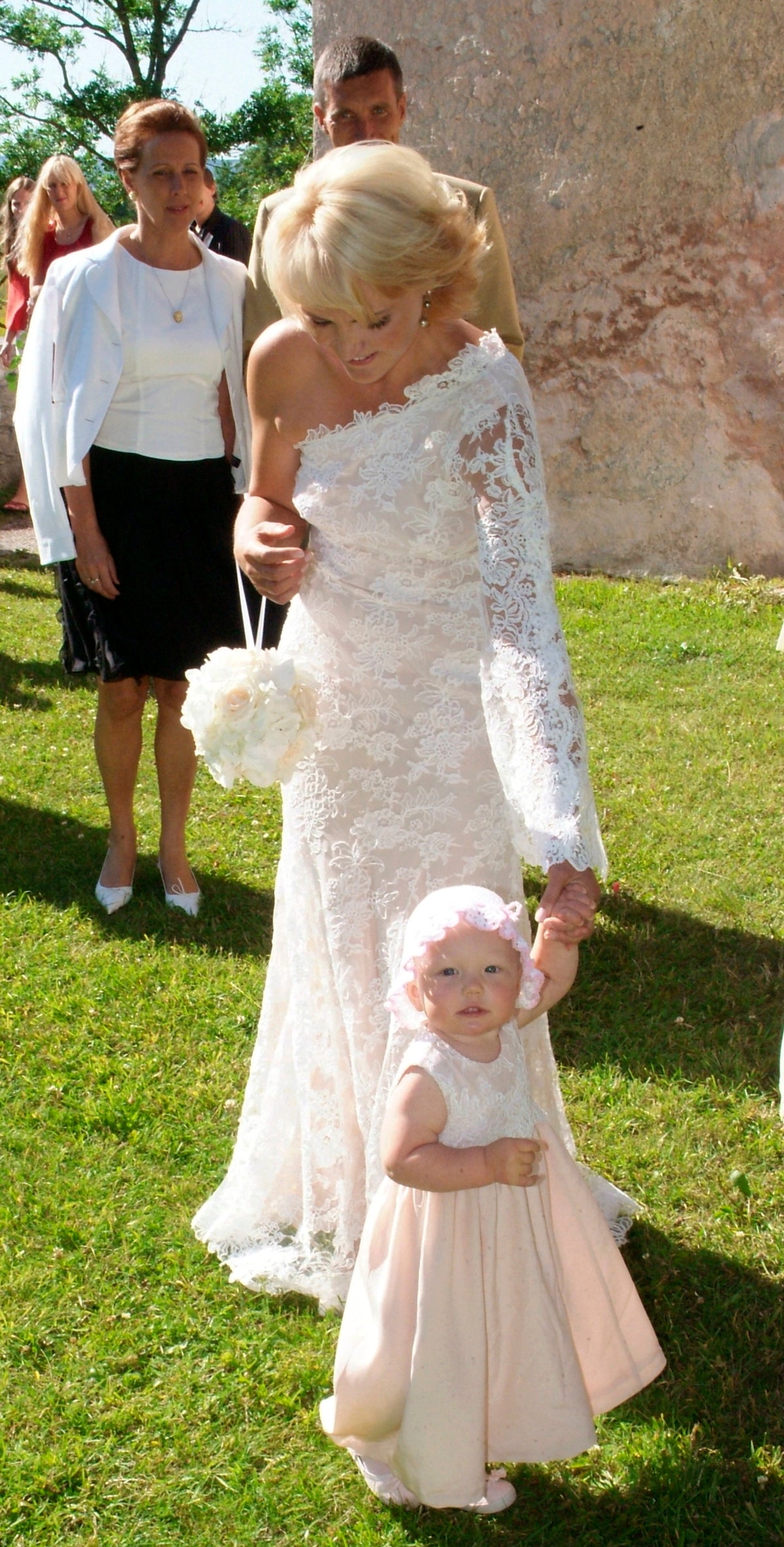 Bride in a lace gown walking with a child at her wedding