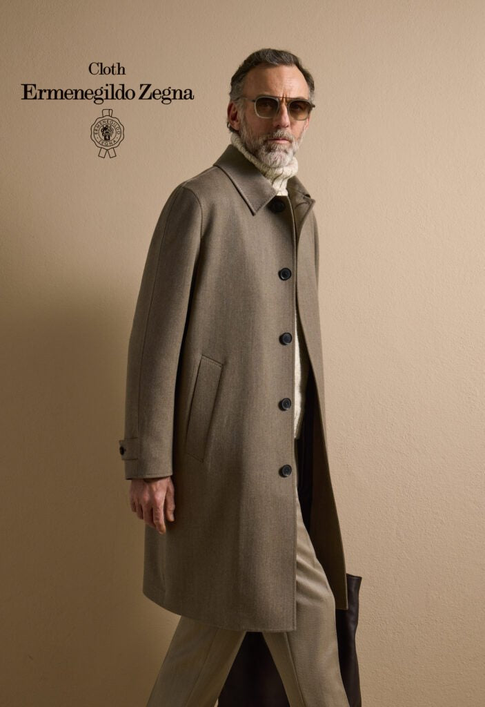 Man wearing a long coat with Ermenegildo Zegna branding on a beige background